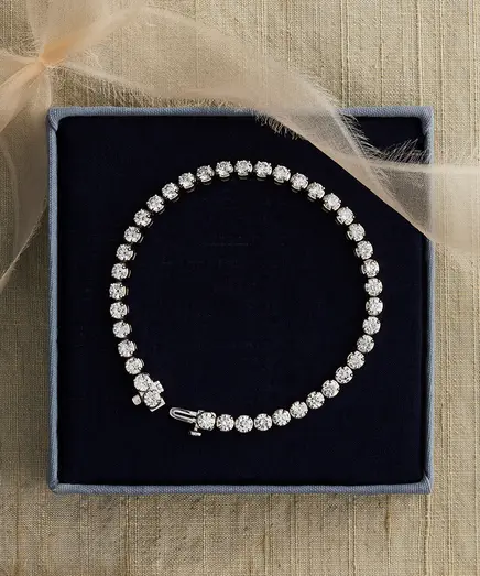 A diamond tennis bracelet displayed in a navy jewelry tray on linen