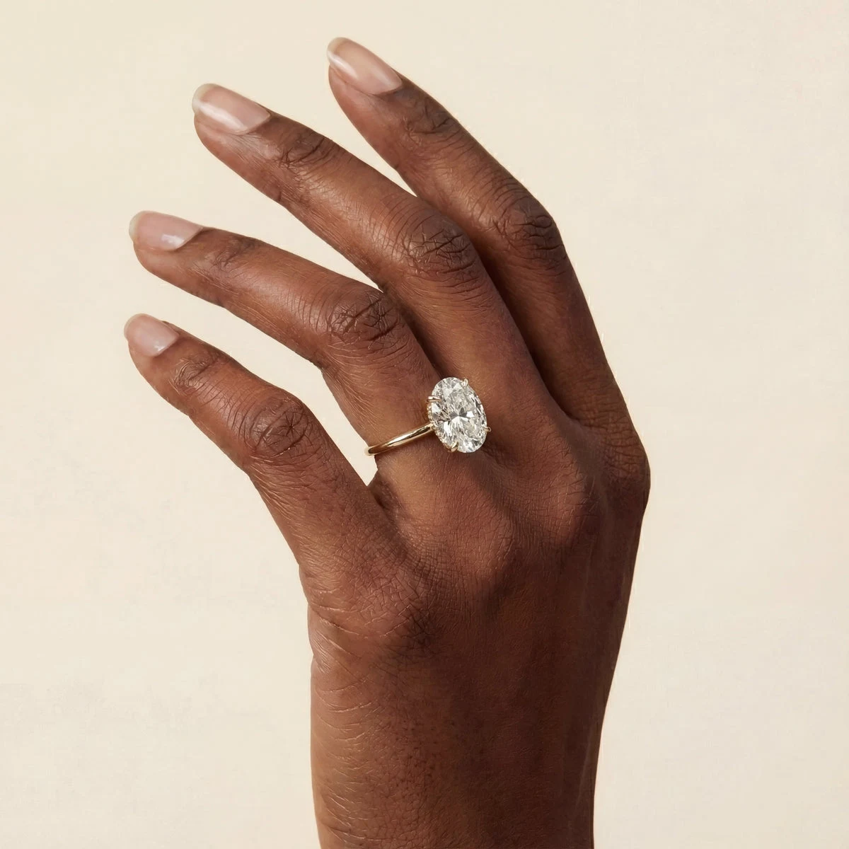 An oval diamond ring with a gold band worn on a hand in natural light